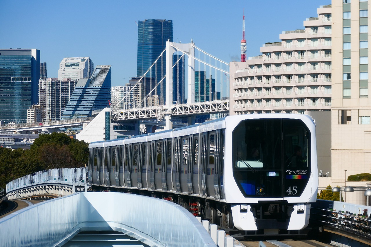 Yurikamome 7300 series 7451 formation entering Tokyo International Cruise Terminal Station. In the background is Tokyo Rainbow Bridge and the skyscrapers of Minato Ward.
