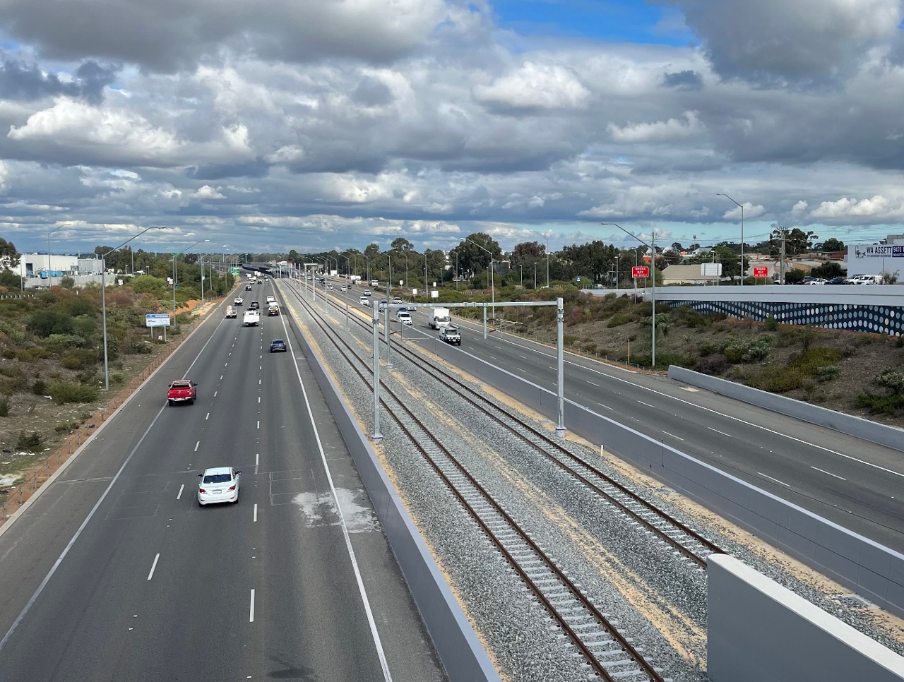 View of the Morley–Ellenbrook Line facing south from the Collier Road bridge over Tonkin Highway in Bayswater, Western Australia, June 2024. The railway line was nearing the end of construction at the time, with workers working on the overhead lines.