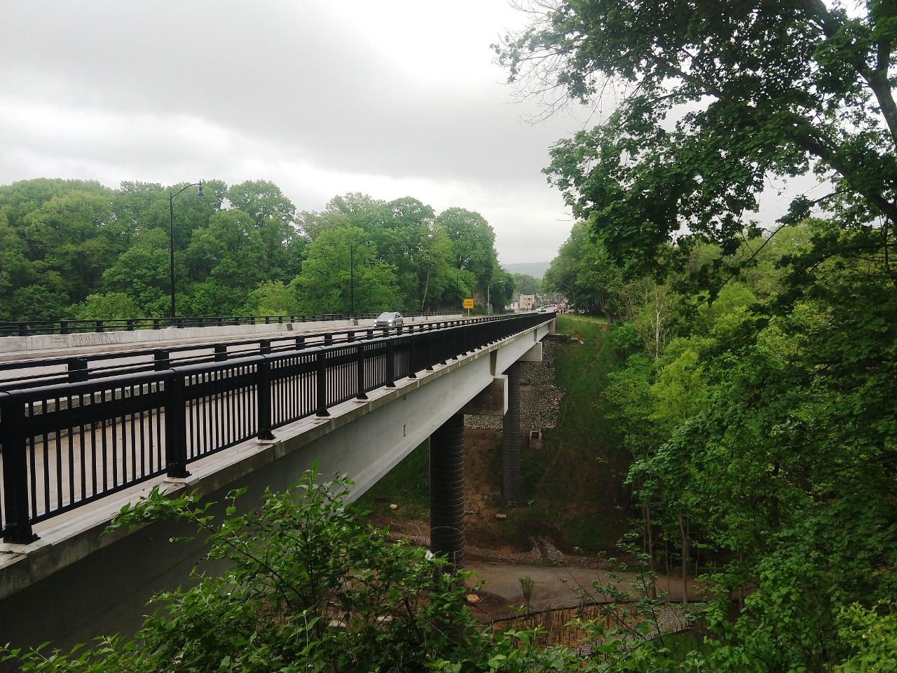 Photo of the Fern Hollow Bridge (2022) within Frick Park in Pittsburgh, Pennsylvania. Photo taken looking west-northwest from the Frick Park shack at the west end of the bridge.