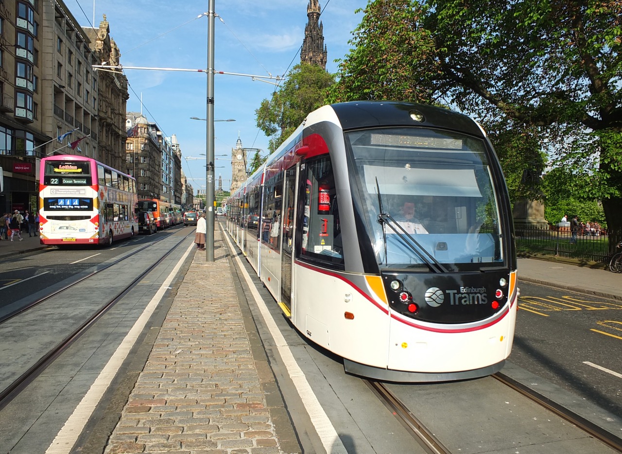 One of the Edinburgh Trams heading west along Princes Street, on the day the line was opened to the public. It's approaching the Hanover Street/Mound junction, beyond which is the Princes Street stop. Heading the other way are some Lothian Buses.