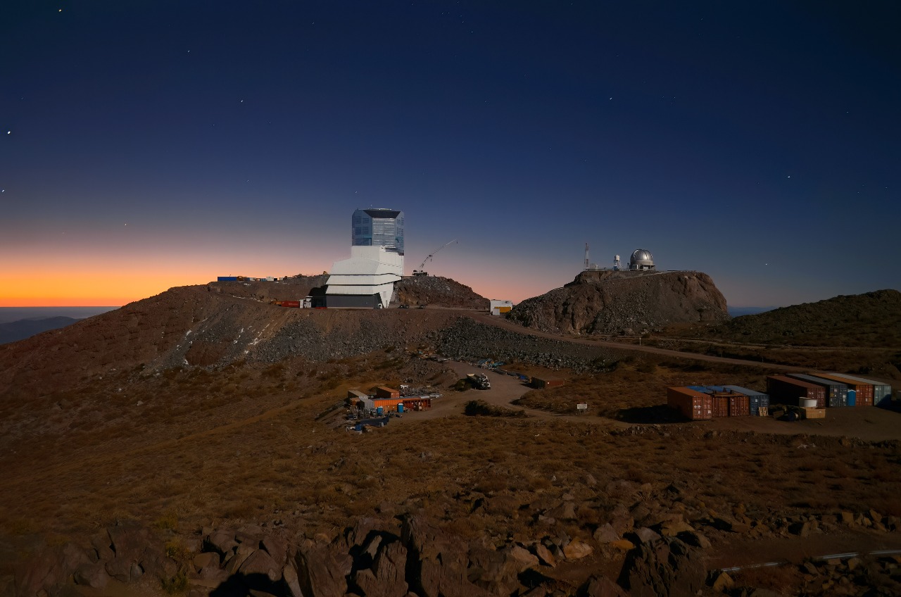 This image shows Vera C. Rubin Observatory, a Program of NSF’s NOIRLab, beneath a late-twilight sky. Rubin is being built to conduct the Legacy Survey of Space and Time (LSST). This survey will observe the entire visible southern sky every few nights over the course of a decade, capturing about 1000 images of the sky every night and giving us a new view of our evolving Universe. The LSST is set to probe four areas of science, one of which is mapping the Milky Way to answer questions about its st